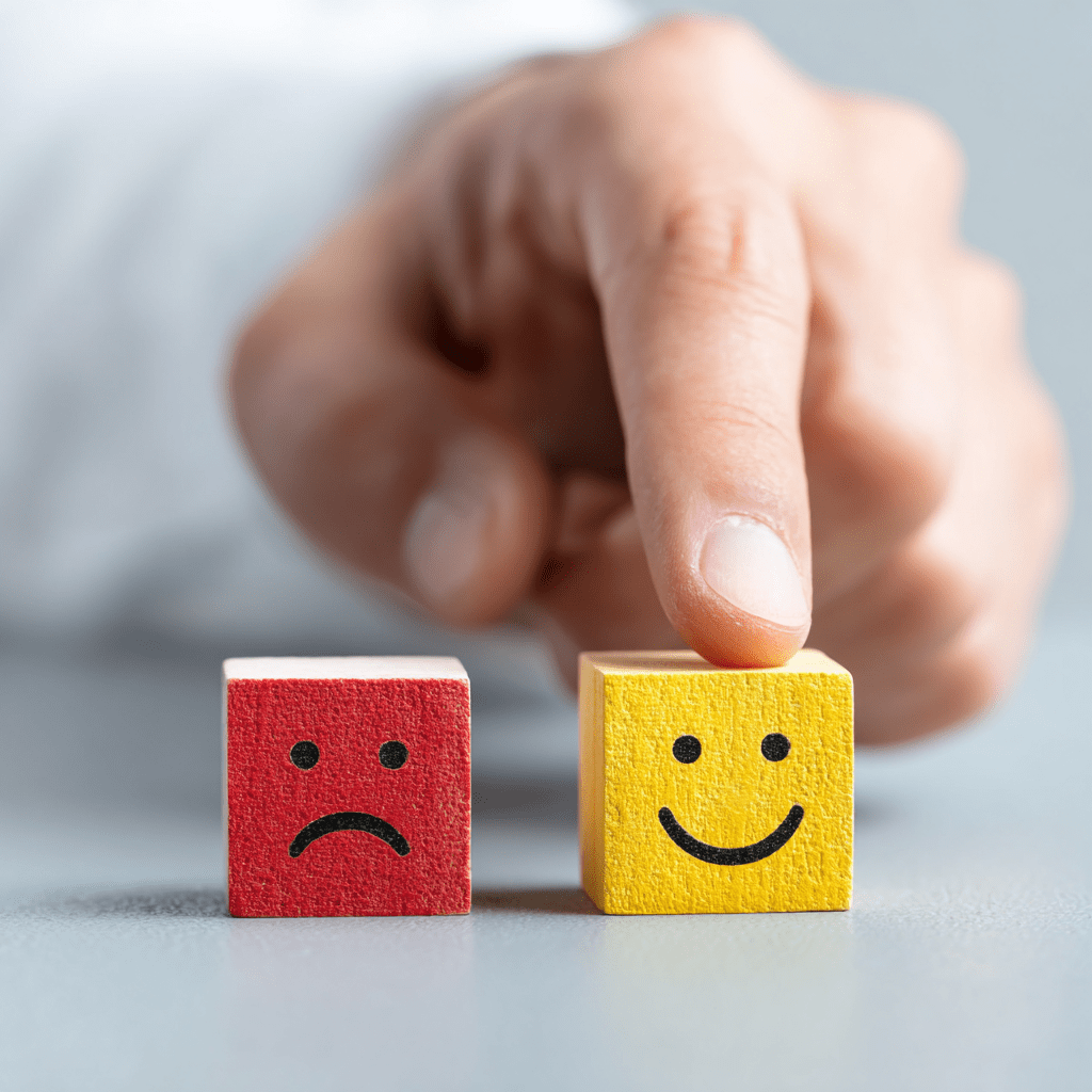 ​​Main choisissant un cube jaune avec un sourire à côté d’un cube rouge triste, symbolisant le rebond et la transition de carrière réussie